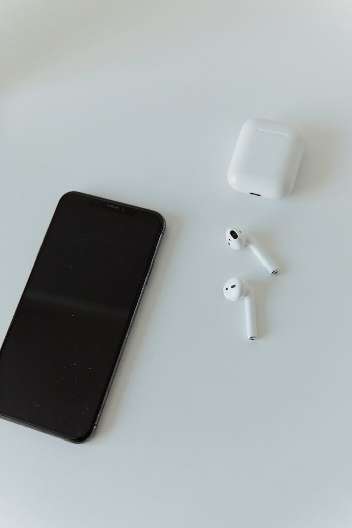 A modern smartphone and wireless earphones on a minimalist white table, embodying contemporary technology.